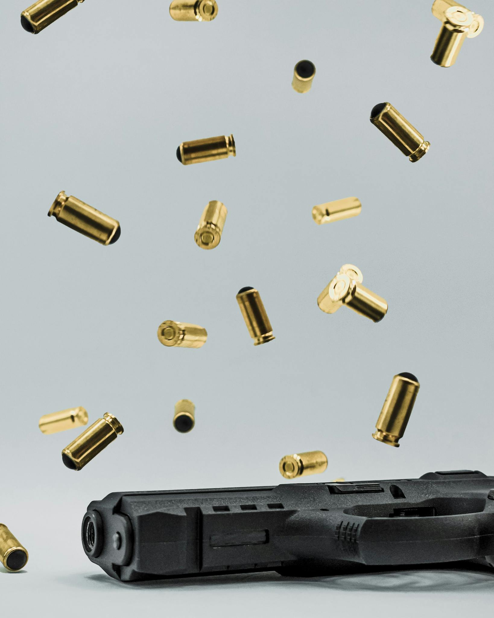 Close-up of a Glock pistol with spent shell casings suspended in the air on a gray studio background.