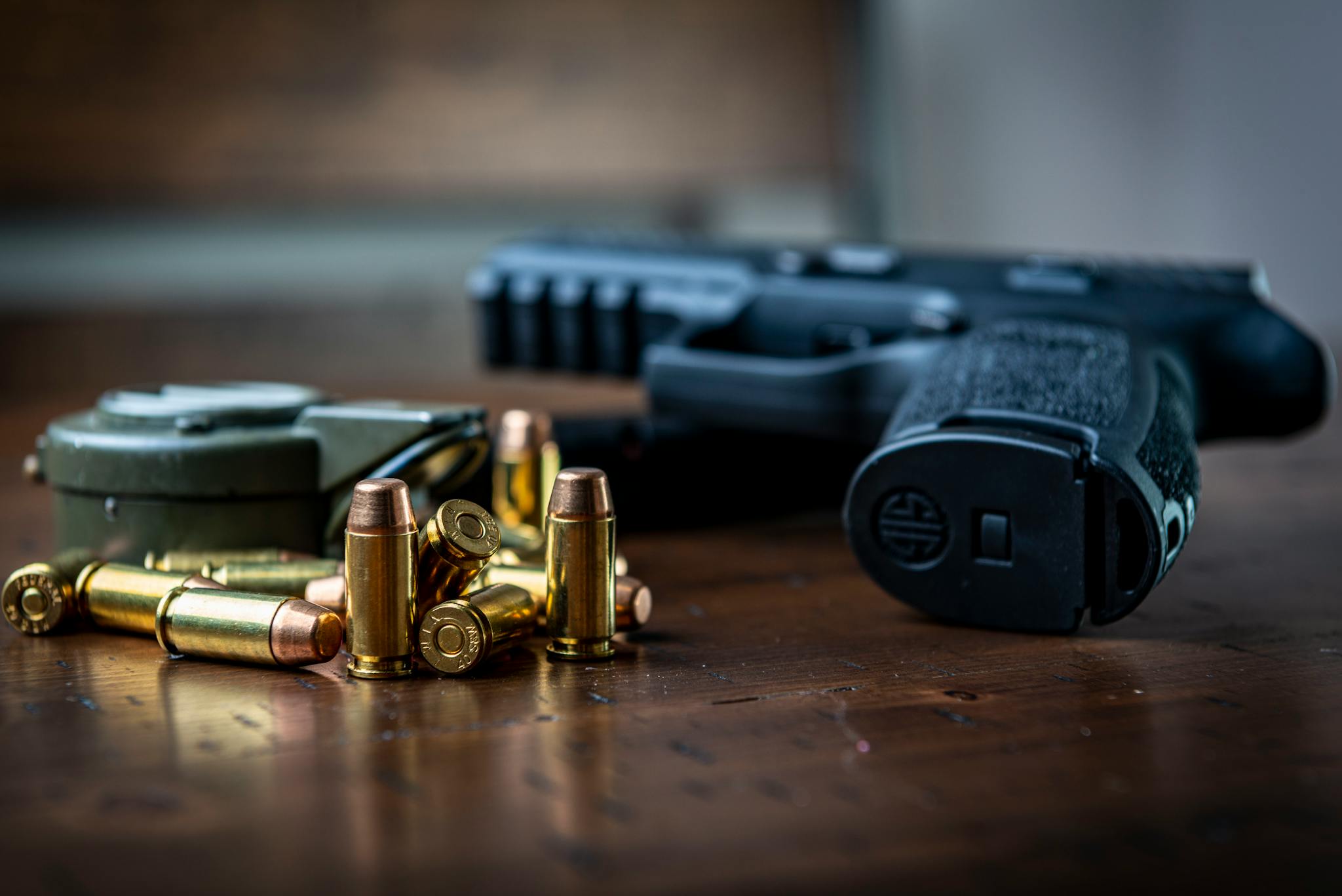 Close view of a handgun with bullets on a wooden surface, emphasizing firearms and ammunition.